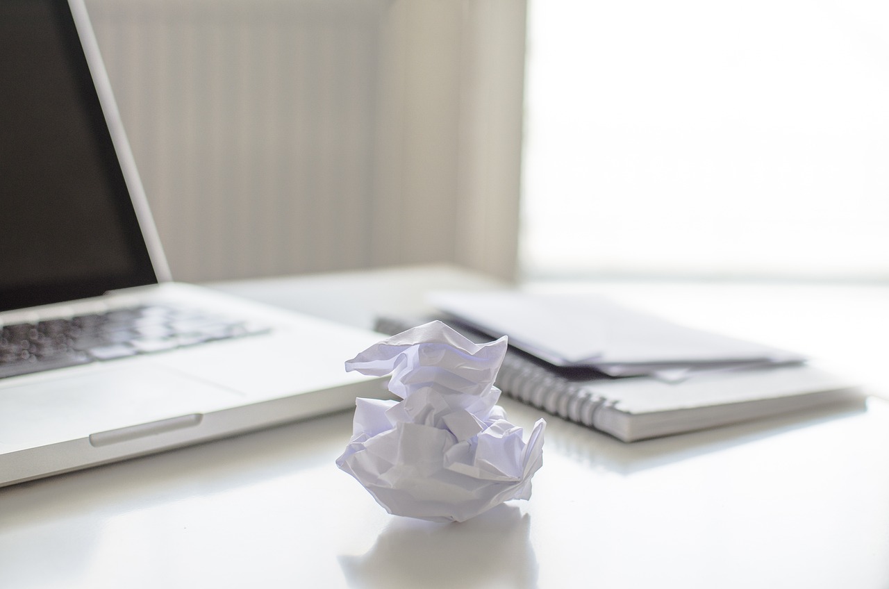 A notebook and open laptop are in the background with a crumpled piece of paper in the foreground.